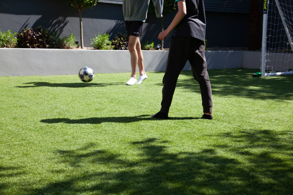 Two boys playing football on an artificial grass lawn.