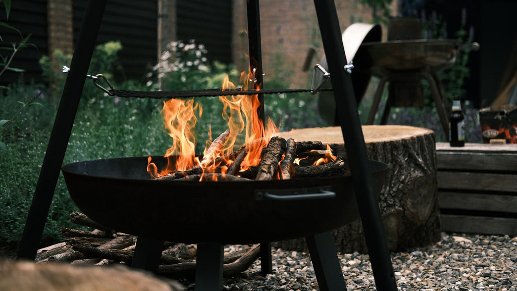 Lit black fire pit in outdoor garden area with stones.