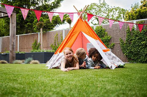 Three children lying in orange tent in summer garden.
