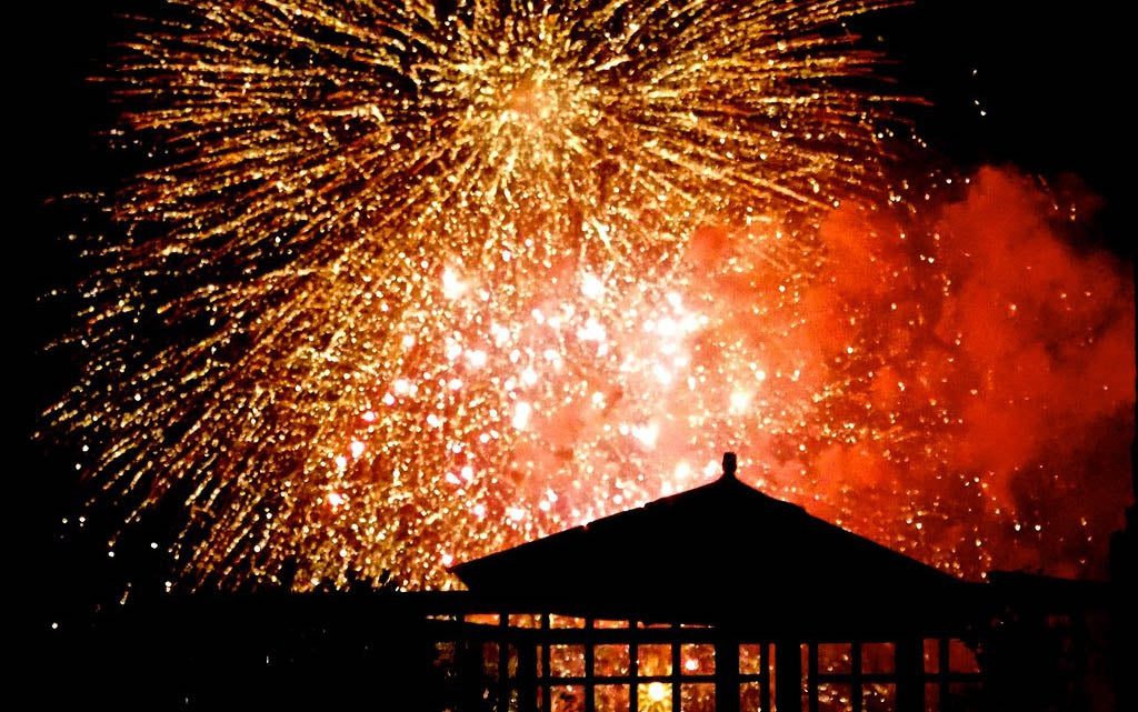 Garden pergola silhouette with light firework explosions behind.
